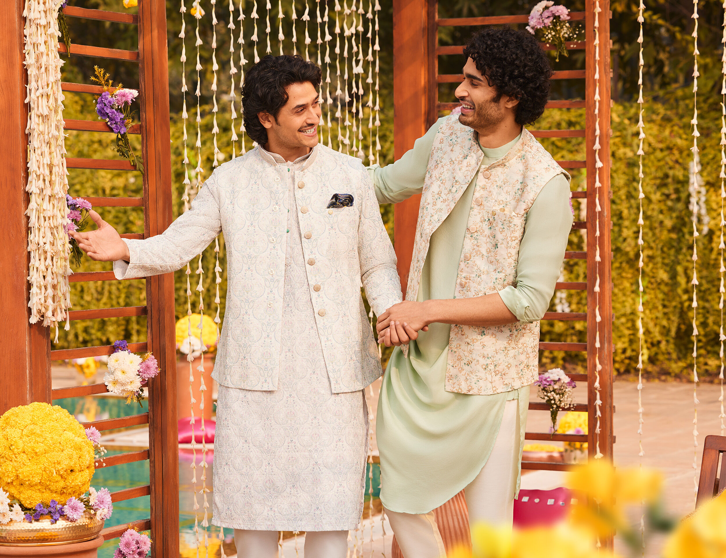 Two friends laughing, one in a white kurta and the other in a light green kurta, at an outdoor wedding event